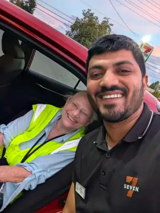Jeana Moore leaning out of a car window, laughing, next to a young man in a 7-Eleven uniform taking the photograph.