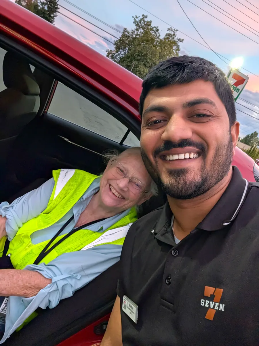 Jeana Moore leaning out of a car window, laughing, next to a young man in a 7-Eleven uniform taking the photograph.