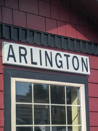 A white board lettered Arlington in tall black capitals on a red wooden wall, above a paned window in which a sign reading Arlington Hardware shows in reverse.
