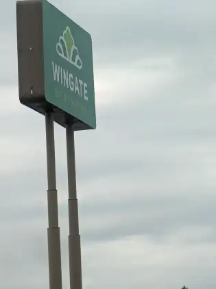 A tall Wingate by Wyndham sign on two steel poles, standing against a flat grey sky.
