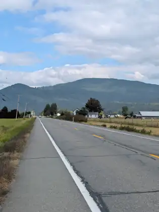 A road running away toward a mountain, with farm buildings and telegraph poles along one side.