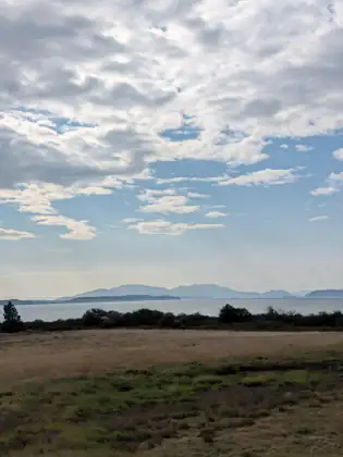The bay and a line of low islands seen across a flat field, under bands of grey and white cloud.