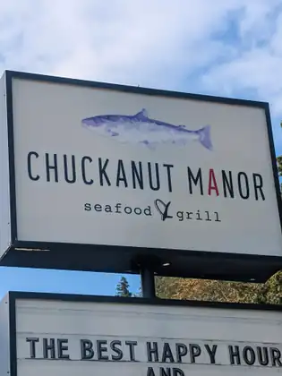 A roadside sign with a painted salmon above the words Chuckanut Manor, seafood grill.