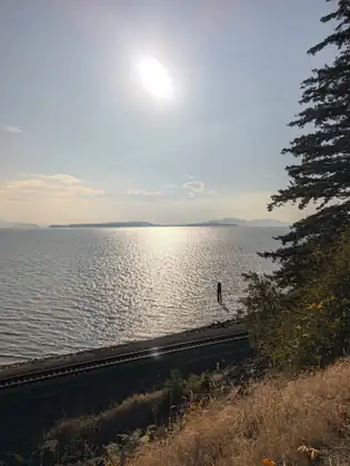 The sun high over the bay, the water silver-white below a road and a railway line cut into the hillside.