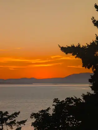 A band of deep orange sky above the dark ridge of an island, the sun gone and the water still.