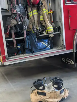 Firefighting turnout gear and boots stowed in the open side locker of a fire engine.