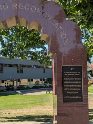 One leg of a red granite arch, its bronze plaque headed 1907: In memory of immigrants from India driven out by mob riots.
