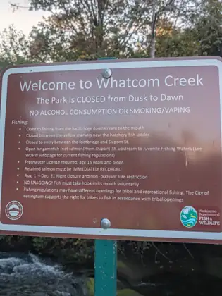 A brown park sign reading Welcome to Whatcom Creek, the park closed from dusk to dawn, with the fishing rules listed underneath.