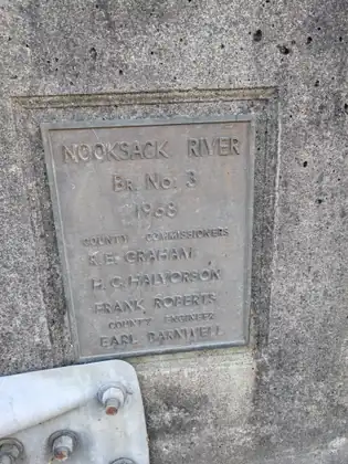 A worn metal plaque set into a concrete bridge, reading Nooksack River, Bridge No. 3, 1968, with the names of the county commissioners and the county engineer.