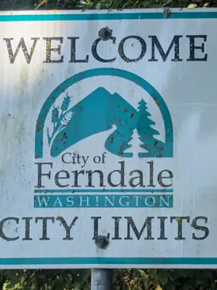 A weathered sign reading Welcome, City of Ferndale, Washington, City Limits, with a mountain and evergreens in the city logo.
