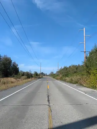 A straight two-lane road running into the distance under power lines and a clear blue sky.