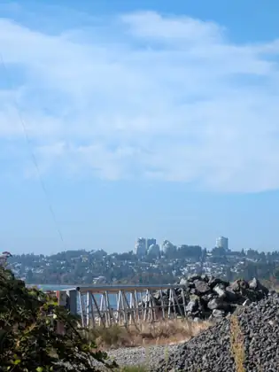 Across the water, a hillside town in Canada with apartment towers on the skyline, seen over a breakwater of big dark boulders and a galvanised steel railing.