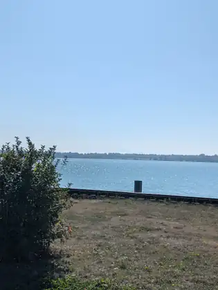 Rough grass and a railway line running along the shore, the bay bright blue and glittering beyond.