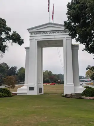 The Peace Arch itself, white against the trees, the words CHILDREN OF A COMMON MOTHER carved across it.