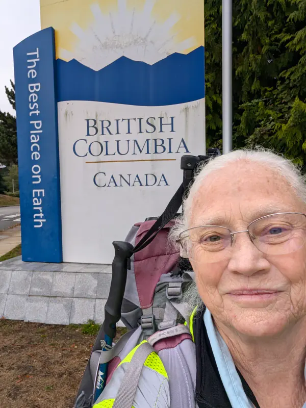 Jeana beside the British Columbia welcome sign, her pack on, smiling into the camera, on September 23, 2026.