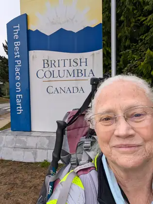Jeana beside the British Columbia welcome sign, her pack on, smiling into the camera.