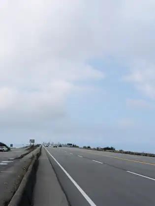 The long, straight causeway road out to the ferry terminal under a pale sky, a concrete barrier along its edge.