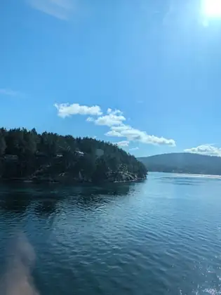 A forested island and calm blue water seen from the ferry, a few white clouds over the hills beyond.