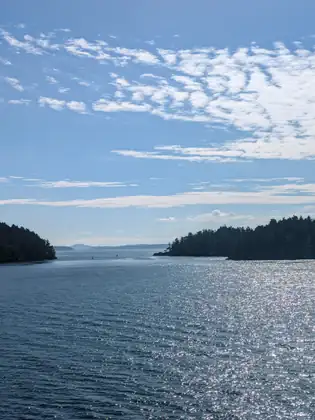 Two forested islands framing a channel of sparkling water, under a wide blue sky full of fine cloud.