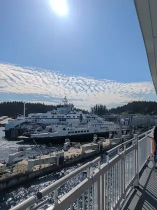 Two white BC Ferries vessels, the nearer one named Skeena Queen, berthed at a terminal dock, seen past the deck railing under a sky of rippled cloud.