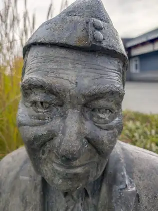 A close view of a weathered grey statue of a smiling older man in a cap.