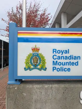 A Royal Canadian Mounted Police sign with the force's crest, a tree with red leaves behind it.