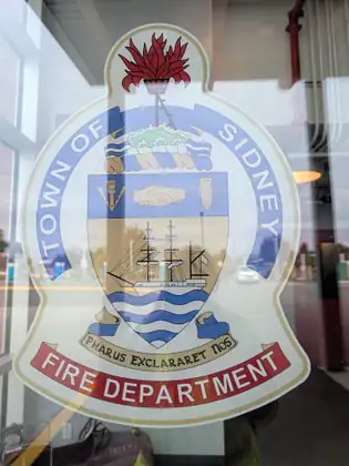 The crest of the Town of Sidney Fire Department on a glass pane, a tall-masted ship on blue waves at its centre.
