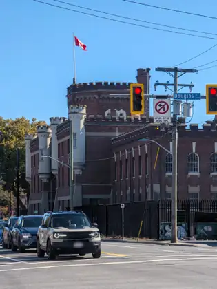 The same castle-like brick building seen across an intersection, with red traffic lights, a Douglas St street sign, a no-left-turn sign and a line of cars waiting at the light.