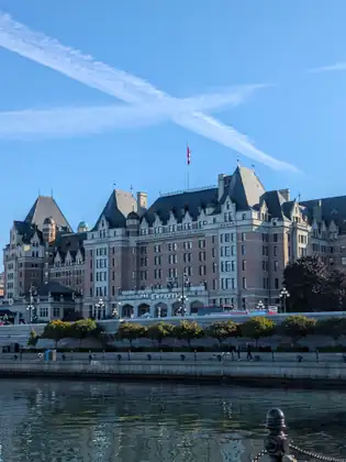 The château-style Empress hotel, its name lettered over the entrance, rises above the harbour seawall under a blue sky crossed by two jet contrails forming an X.