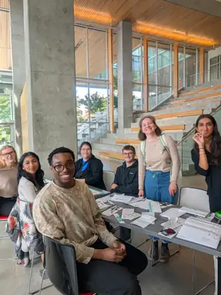 Seven students smile for the camera around the swab-kit table in the atrium, one young woman on the right holding up her swab.