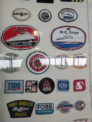 A framed display of embroidered maritime patches, including Black Ball Line, M.V. Coho, Grays Harbor Bar Pilot, Todd Shipyards, Foss, Victoria Clipper and Port Angeles Pilots.