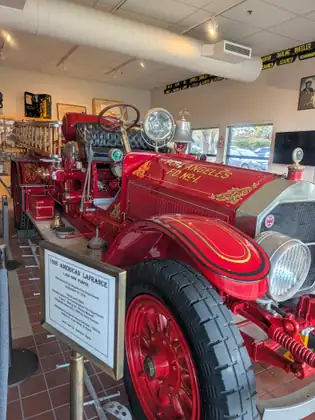 A restored red 1926 American LaFrance fire engine lettered Port Angeles F.D. No. 1, with gold-leaf trim, silver headlamps, a searchlight and an eagle-topped bell, stands indoors beside an information placard.