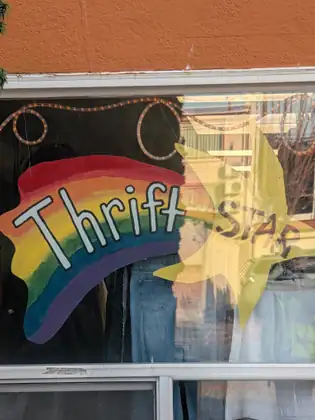 A shop window painted with a rainbow and a yellow star reading Thrift Star, with jeans and other clothes on display behind the glass.