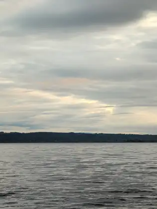 Calm grey water stretches to a dark line of distant shore under a layered evening sky.