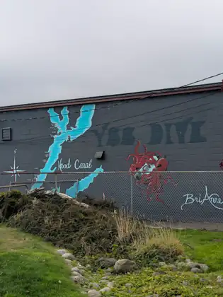 A mural on a grey cinder-block wall maps Hood Canal as a bright turquoise ribbon, with a red octopus painted beside it, above a strip of grass and stones.