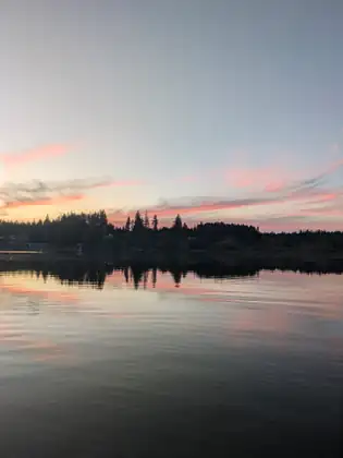 Pink clouds drift above the tree line across the lake, mirrored in the calm water.