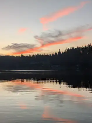 Streaks of pink and grey cloud sweep across the evening sky above the dark shoreline, reflected in the lake.