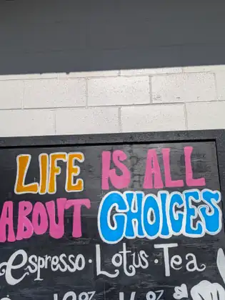 A colourful hand-painted sign on a coffee stand reads “Life is all about choices”, above “Espresso · Lotus · Tea”.