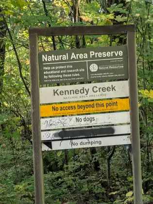 A Kennedy Creek Natural Area Preserve sign in the woods, reading No access beyond this point, No dogs and No dumping.