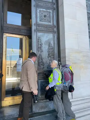 Jeana stands by the Capitol entrance beside a man in a tan jacket.