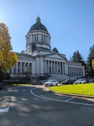 The domed Washington State Capitol at the end of a curving drive, with autumn trees and parked cars.