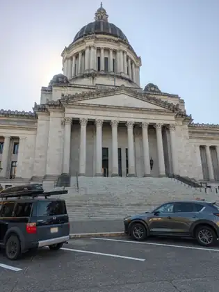 The Capitol’s columned front and broad steps, with parked cars in the foreground.