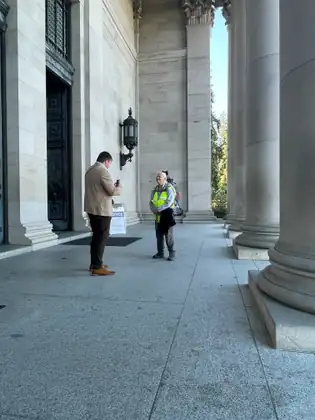 Beneath the Capitol’s tall columns, Jeana in her safety vest talks with a man in a tan jacket.
