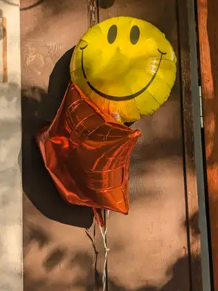 A yellow smiley-face balloon and an orange star balloon tied up against a wooden wall.