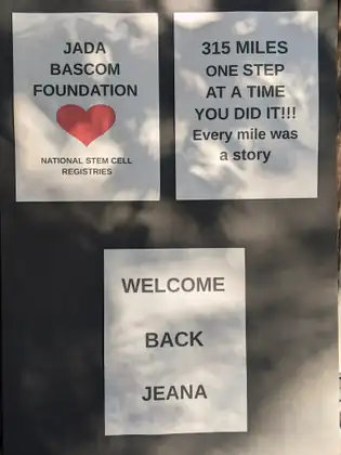Signs on a door read “Jada Bascom Foundation, National Stem Cell Registries”, “315 miles, one step at a time. You did it!!! Every mile was a story” and “Welcome back Jeana”.