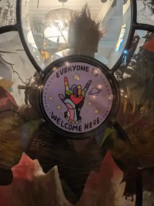 A round sticker on a window reads “Everyone is welcome here” around a rainbow-coloured hand.
