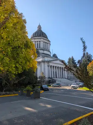 The Washington State Capitol dome and columns appear through golden autumn leaves.