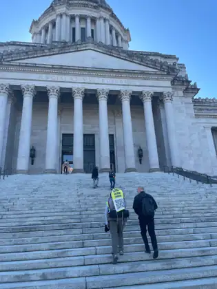 Jeana climbs the broad outdoor steps toward the Washington State Capitol, with another person beside her.