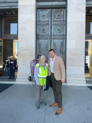 Jeana and a man in a tan jacket smile together outside the Capitol doors.